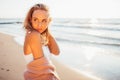 Headshot of beautiful blonde slim girlwearing white dress and cardigan on beach of sea or ocean against the sun. Youth Royalty Free Stock Photo