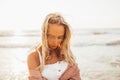 Headshot of beautiful blonde slim girlwearing white dress and cardigan on beach of sea or ocean against the sun. Youth Royalty Free Stock Photo