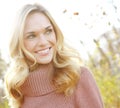 Headshot of a beautiful blonde woman standing in a park in fall. Happy attractive young female smiling outside on an