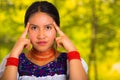 Headshot beautiful young woman wearing traditional andean blouse with red necklace, posing for camera touching face Royalty Free Stock Photo