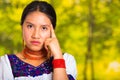 Headshot beautiful young woman wearing traditional andean blouse with red necklace, posing for camera touching face Royalty Free Stock Photo