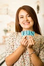 Headshot charming brunette woman holding up small letters spelling the word fun and smiling to camera Royalty Free Stock Photo