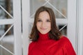 Headshot of charming woman with dark hair, wears knitted sweater, looks directly at camera, has friendly smile, poses indoor, has