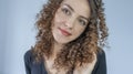 Headshot of a cheerful girl with curly hair in a black T-shirt with a smile, against a gray background. Perming a