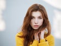 Headshot of fabulous redhead woman with long hair in yellow sweater having fun on grey concrete wall background with sun light