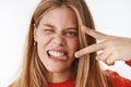Headshot of funny emotive and charismatic young carefree girl making faces sticking out tongue showing peace gesture and