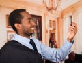 Headshot handsome man wearing business suit taking a selfie with mobile phone, as seen from profile angle, lobbby Royalty Free Stock Photo