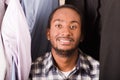 Headshot handsome young man standing inside wardrobe with clothes sorrounding, smiling to camera