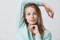 Headshot of happy pleased blonde girl of European appearance with dark eyes wearing blue long-sleeved top looking and