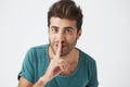 Headshot of happy unshaven smiling hispanic man in casual clothes, holding index finger at lips, asking his girlfriend