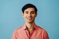 Headshot hispanic latino man black hair smiling handsome young adult wearing pink shirt over blue background looking at Royalty Free Stock Photo