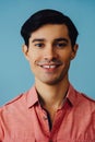 Headshot hispanic latino man black hair smiling handsome young adult wearing pink shirt over blue background looking at Royalty Free Stock Photo