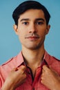 Headshot hispanic latino man black hair smiling handsome young adult wearing pink shirt over blue background looking at Royalty Free Stock Photo