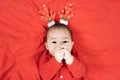 Headshot of 6 months old cute newborn baby boy wearing christmas antlers of a deer on a red blanket.Looking at camera. Holiday Royalty Free Stock Photo