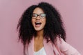 Headshot of overemotive young curly woman keeps mouth opened, wears optical glasses and formal suit, comes on business meeting,