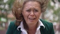 Headshot overwhelmed overburdened plus-size woman crying outdoors on windy day on city street. Close-up desperate