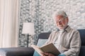 Headshot portrait close up of old happy and relaxed man sitting reading a book at home. Mature male person enjoying free time Royalty Free Stock Photo