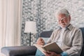 Headshot portrait close up of old happy and relaxed man sitting reading a book at home. Mature male person enjoying free time Royalty Free Stock Photo