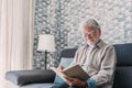 Headshot portrait close up of old happy and relaxed man sitting reading a book at home. Mature male person enjoying free time Royalty Free Stock Photo