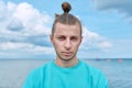 Headshot portrait of serious young male looking at camera, blue sky sea background