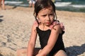 Headshot portrait of cute upset baby girl with wet hair and swimsuit, sitting on the sandy beach on the sea background. Kids Royalty Free Stock Photo