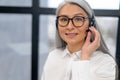 Headshot portrait of a smiling elegant senior lady, wearing headset and glasses looking at the camera. Portrait of a Royalty Free Stock Photo