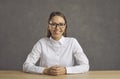 Headshot portrait of young woman at desk looking at camera on studio wall Royalty Free Stock Photo