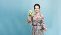 Headshot of pretty young woman with tender smile, healthy skin, carries bouquet of spring flowers, over light blue