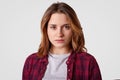 Headshot of serious woman has confident expression, wears checkered shirt, casual t shirt, stands against white background,