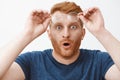 Headshot of shocked and impressed overwhelmed redhead guy with beard, taking off glasses and holding rim on forehead