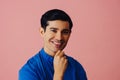 Headshot smiling handsome young adult latino man with hand on chin black hair and blue shirt over pink background