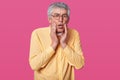 Headshot of stupefied terrified thin man wears yellow shirt, keeps hands on cheeks. Surprised elderly male with glasses against Royalty Free Stock Photo