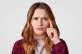 Headshot of thoughtful bothered woman with serious expression keeps index finger on temple, tries to focuse on something, wears Royalty Free Stock Photo