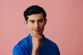 Headshot thoughtful handsome young adult latino man with hand on chin black hair and blue shirt over pink background Royalty Free Stock Photo