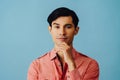 Headshot thoughtful handsome young adult latino man with hand on chin black hair and pink shirt over blue background Royalty Free Stock Photo