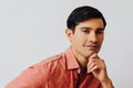 Headshot thoughtful handsome young adult latino man with hand on chin black hair and pink shirt over gray background Royalty Free Stock Photo