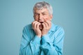 Headshot of wrinkled grey haired man in despair, keeps hands near opened mouth, looks nervously, has grief, wears formal outfit in