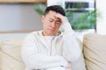 Asian man holding his head with a severe headache at home in a room on the couch. Up close, the casual male