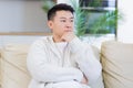 asian man holding his head with a severe headache at home in a room on the couch. Up close, the casual male