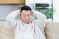 Asian man holding his head with a severe headache at home in a room on the couch. Up close, the casual male