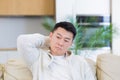 Asian man holding his head with a severe headache at home in a room on the couch. Up close, the casual male