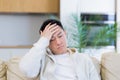 asian man holding his head with a severe headache at home in a room on the couch. Up close, the casual male