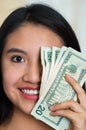 Headshot young brunette woman facing camera, covering one eye with several twenty dollar bills