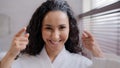 Headshot young happy attractive young curly woman in bathrobe in bathroom touching soft smooth facial skin after beauty