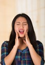 Headshot young hispanic woman touching her cheeks using hands, painful facial expression, injury concept