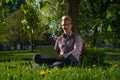 Headshot A young man freelancer is sitting under a tree on a sunny day. working on a laptop