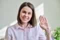 Headshot young smiling woman looking at camera greeting waving hand in home interior