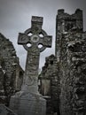 Headstone with celtic cross on a cemetery with church ruins in the background