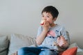 Healhty kid eating an apple while watching TV, Portrait child eating fresh fruit. Happy boy sitting on sofa relaxing at home on