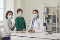 Mother, child and family doctor in face masks looking at camera in hospital office